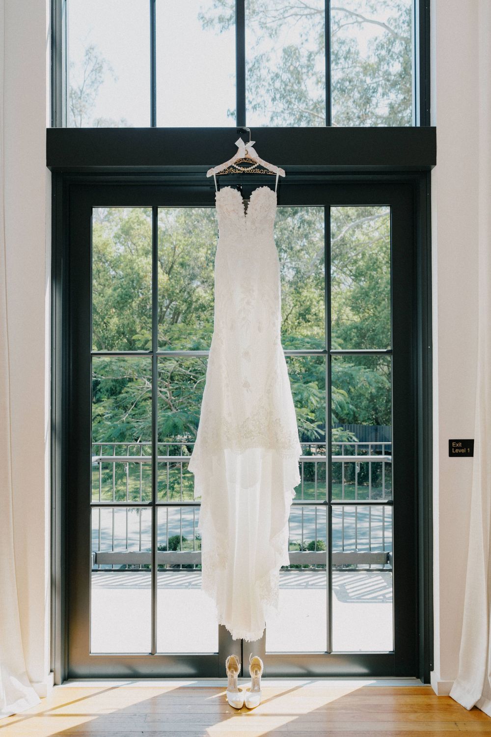 Elegant white wedding dress hanging in front of tall window with natural light.