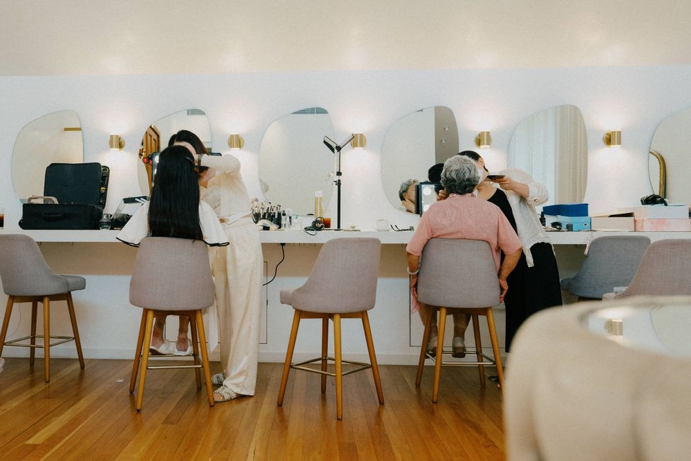Row of makeup stations with pink chairs in bright white salon.