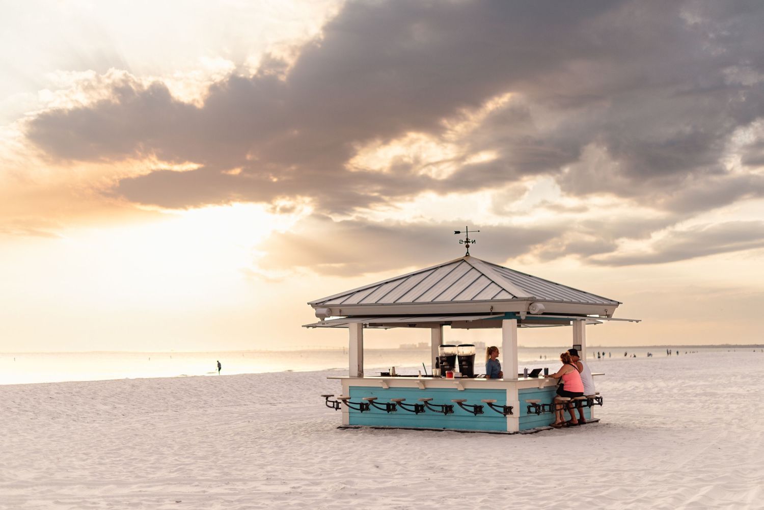 Seaside snack bar pavilion on white sandy beach during a dramatic sunset.