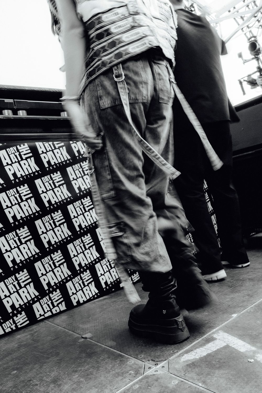 Black and white low angle shot of concert-goers' legs against branded backdrop.
