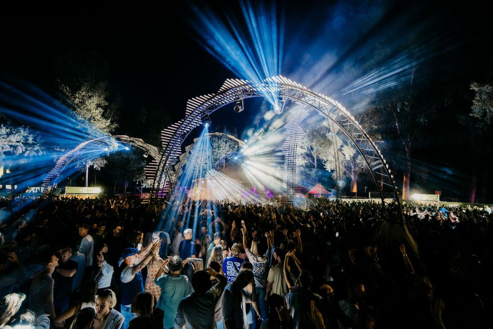 Electric blue laser lights illuminate a packed outdoor concert crowd at night.