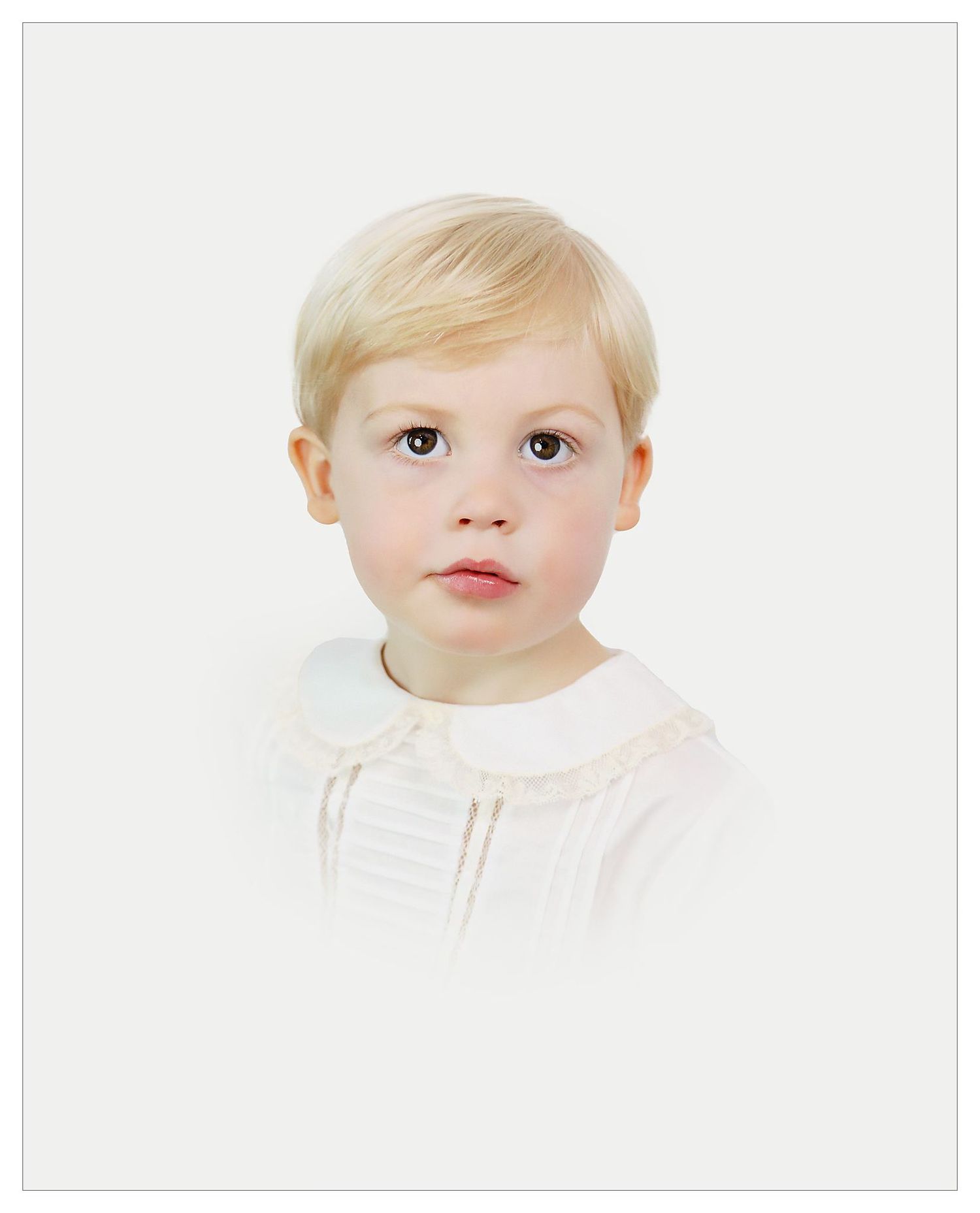 Studio portrait of young child in white collared outfit against white background.