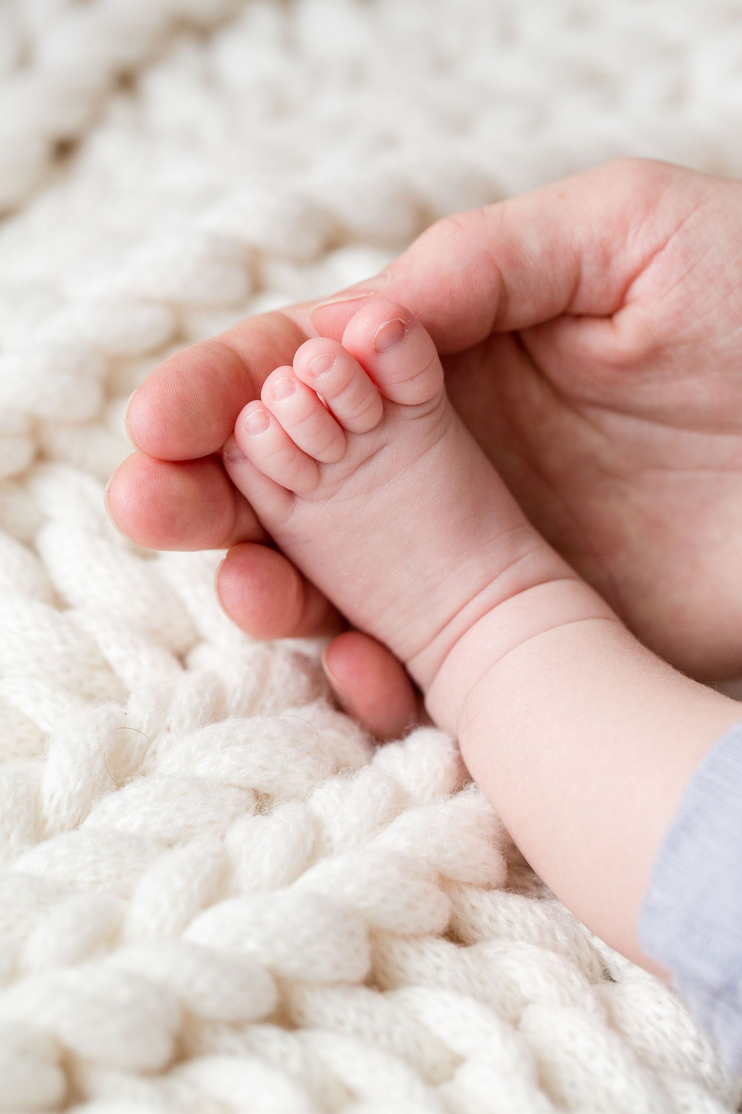 Close up of tiny baby foot being gently held against white knitted blanket background.