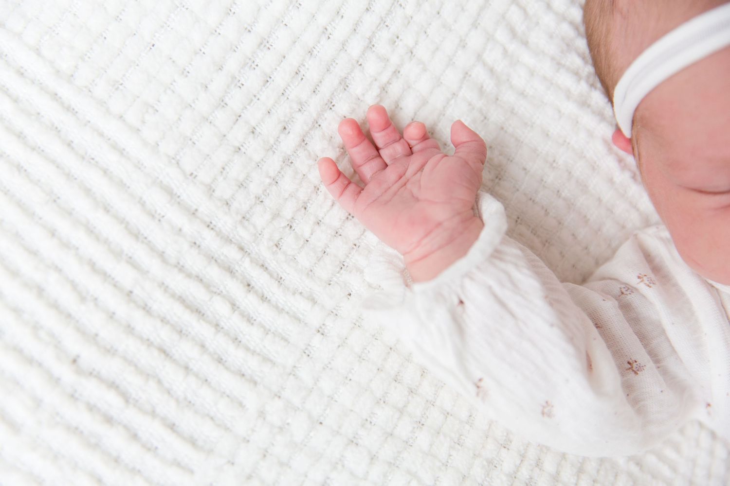 Closeup of newborn baby's tiny hand against white textured blanket.