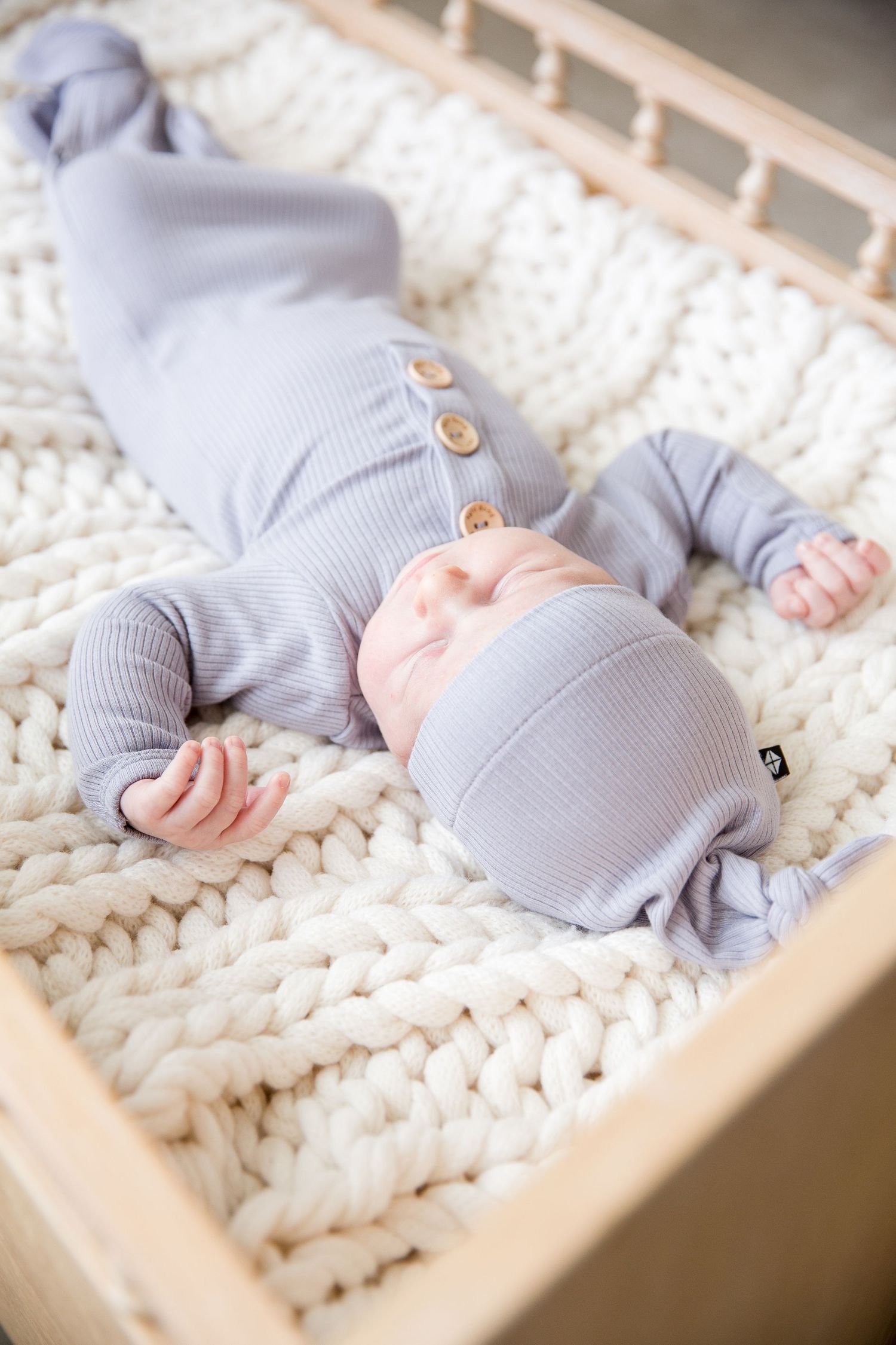 Baby wearing soft gray outfit sleeping on chunky knit blanket.