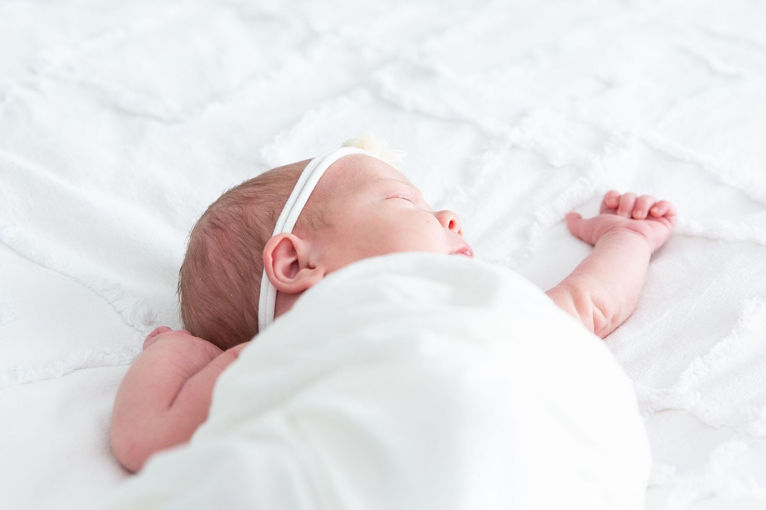 Peaceful newborn baby sleeping while swaddled in white blanket.