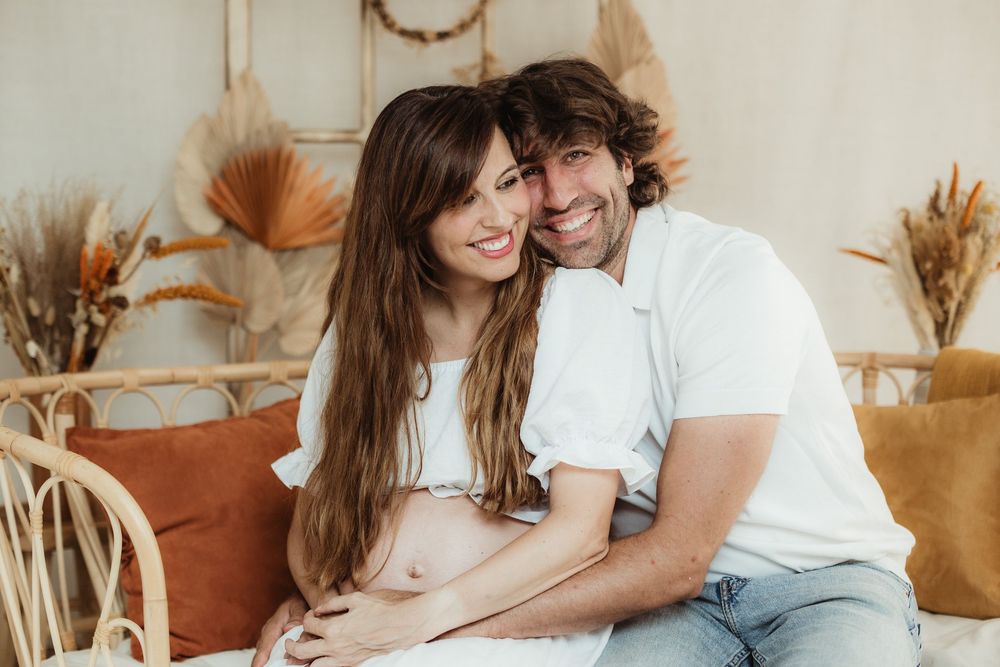 A couple embraces and laughs together while sitting on a brown couch in a cozy living room setting.