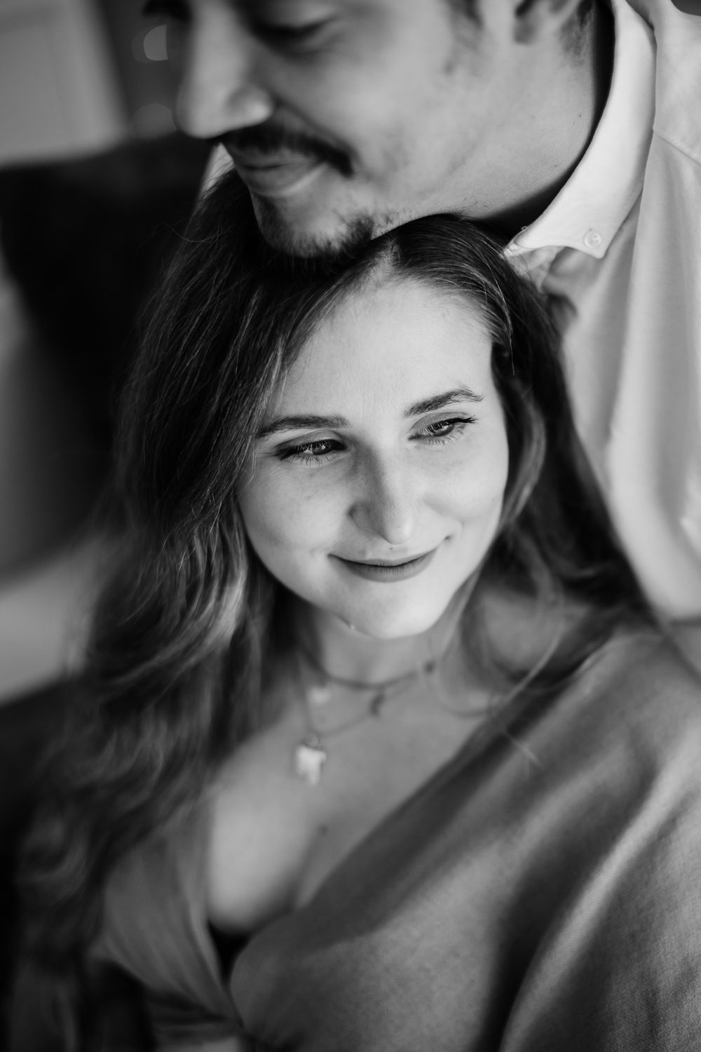 Black and white portrait of a couple sharing an intimate moment with soft smiles and natural lighting.