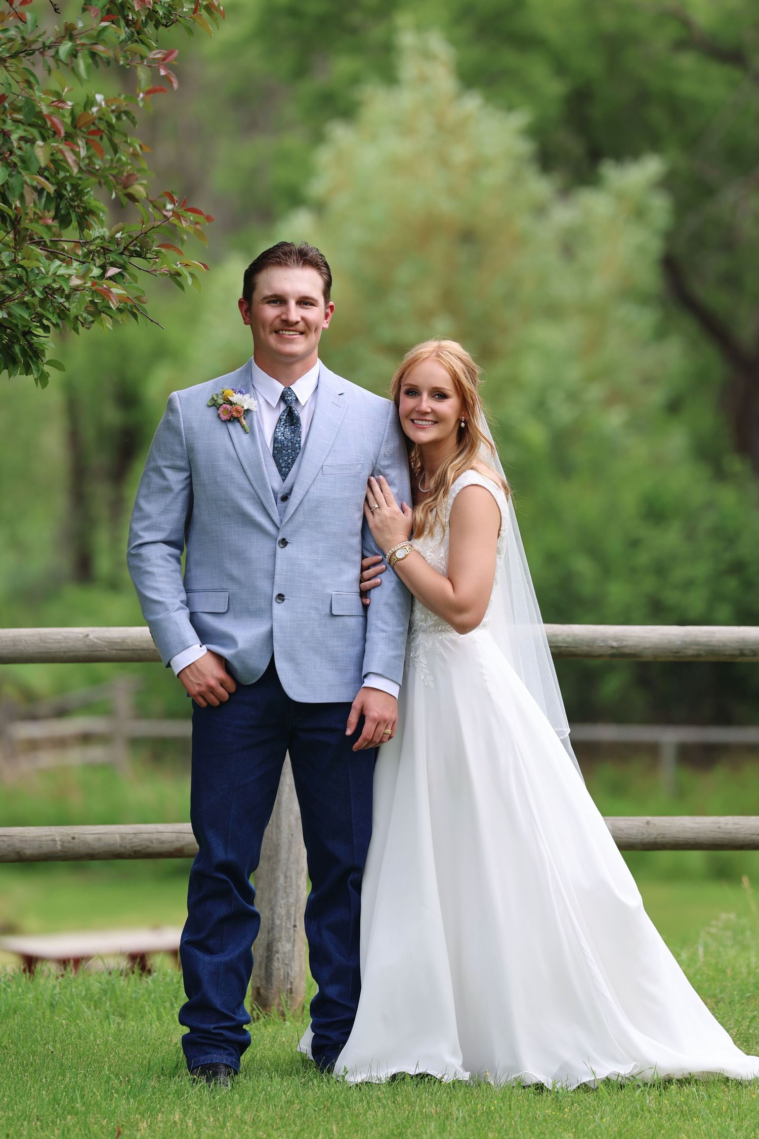 Wedding portrait of a family in formal attire with a white floral bouquet in an outdoor garden setting.