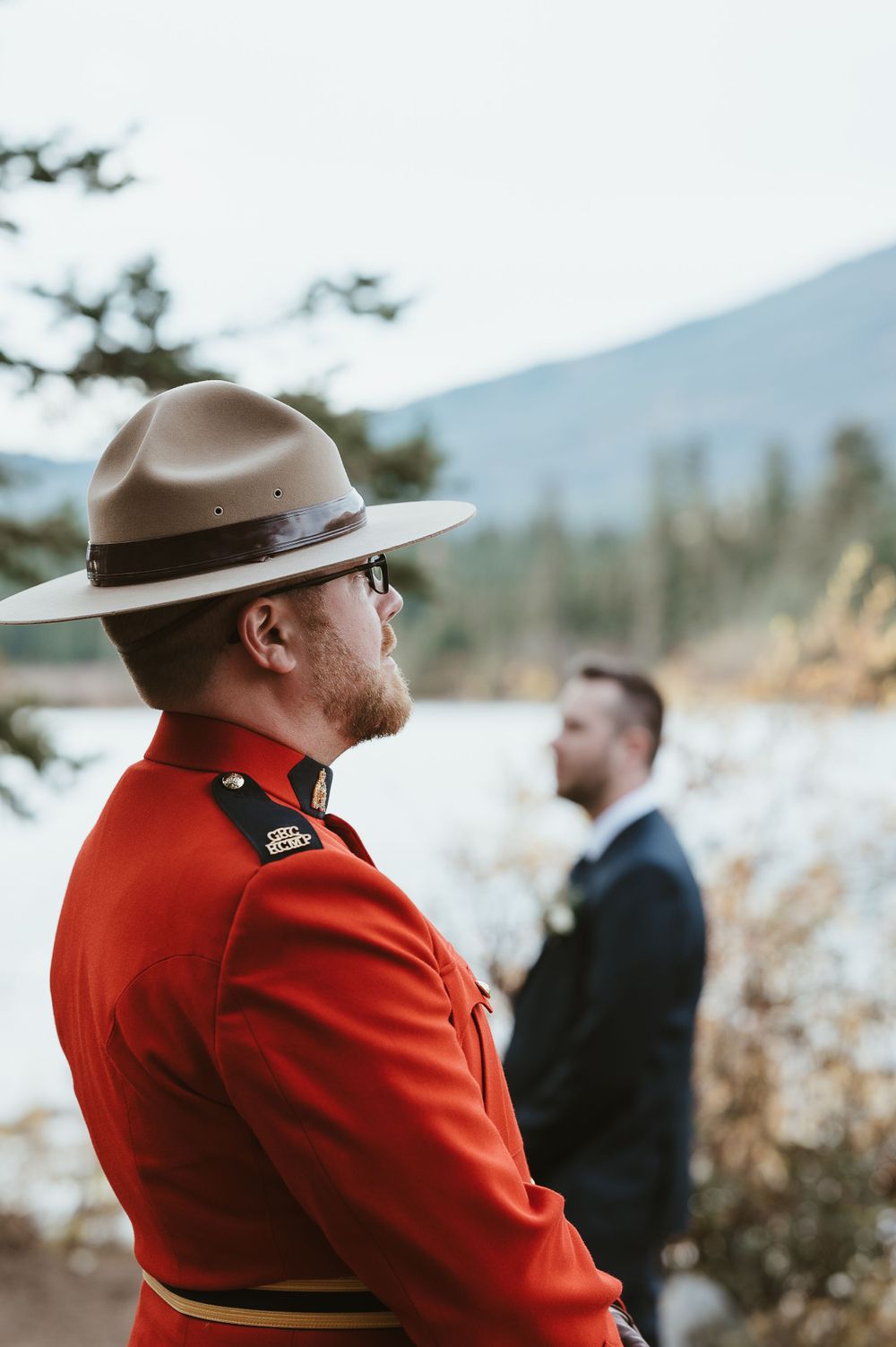 A Royal Canadian Mounted Police officer in red uniform stands watching a mountain ceremony.