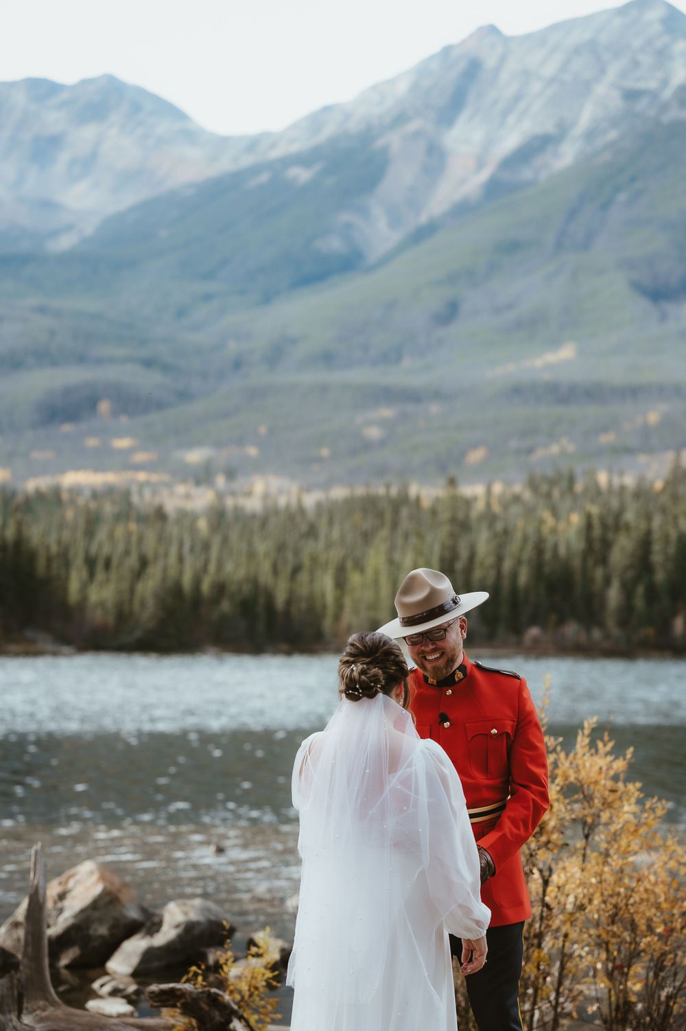 A lakeside wedding ceremony with mountains and evergreen forest creating a stunning backdrop.