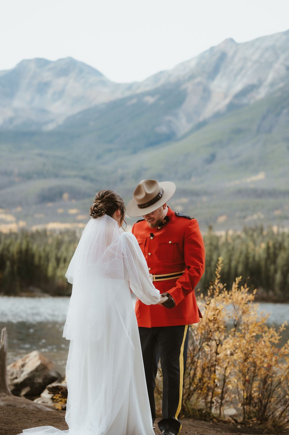 An intimate wedding ceremony by a mountain lake with a Mountie officer in traditional red uniform.