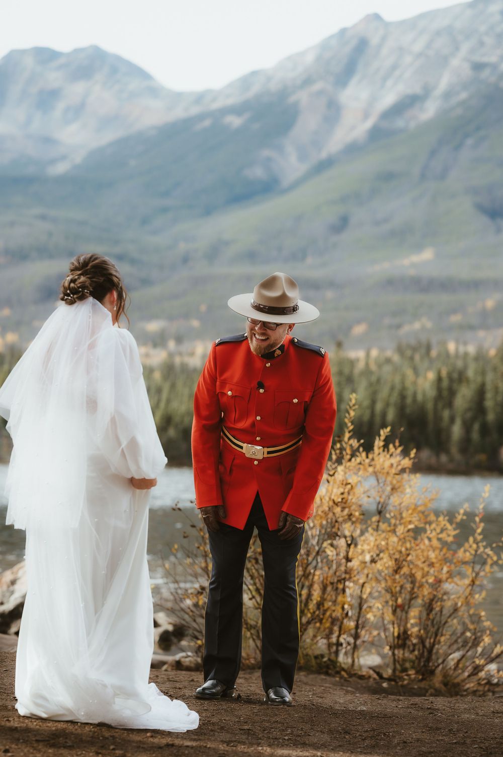 A stunning mountain wedding scene with the couple standing on a rocky overlook above a serene lake.
