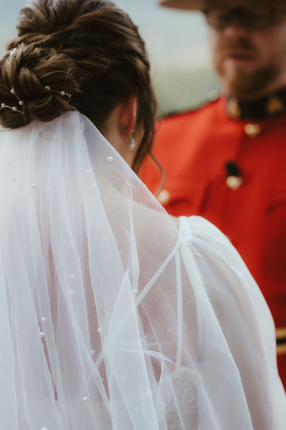 Close-up detail of a wedding veil and red uniform with mountains in the background.