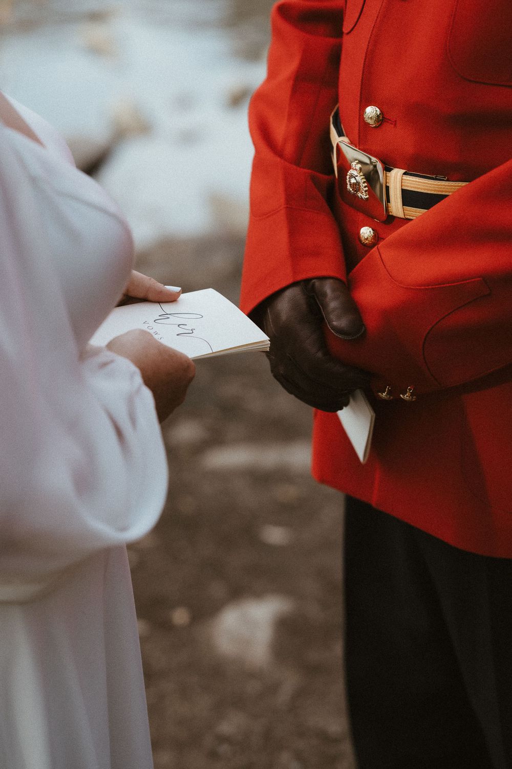 Close-up of hands exchanging wedding vows on paper against a red ceremonial uniform.