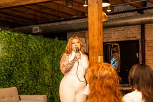 A speaker presents to an audience in an industrial-style venue with exposed brick and wood beams.