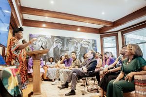 Indoor presentation with audience seated beneath exposed wooden beams and black and white wall mural.