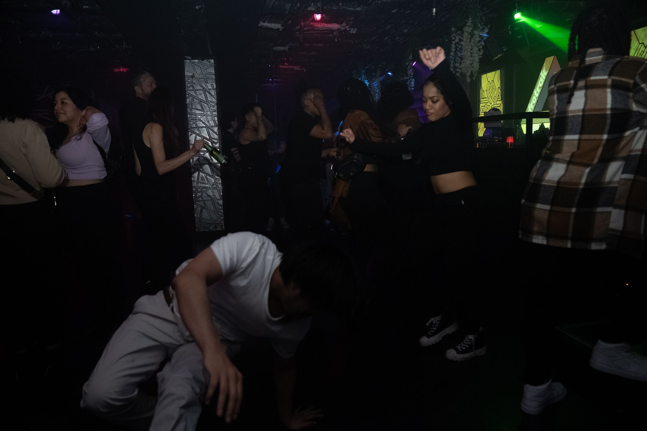 People dancing and socializing in a dark nightclub with green lighting effects.