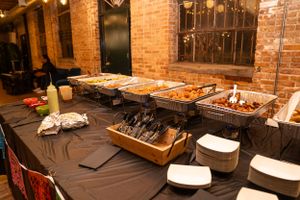 Catering setup with chafing dishes on black tablecloths in a rustic brick venue.