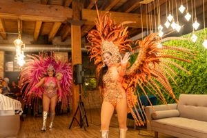 Performers in colorful feathered carnival costumes entertain at an indoor venue.