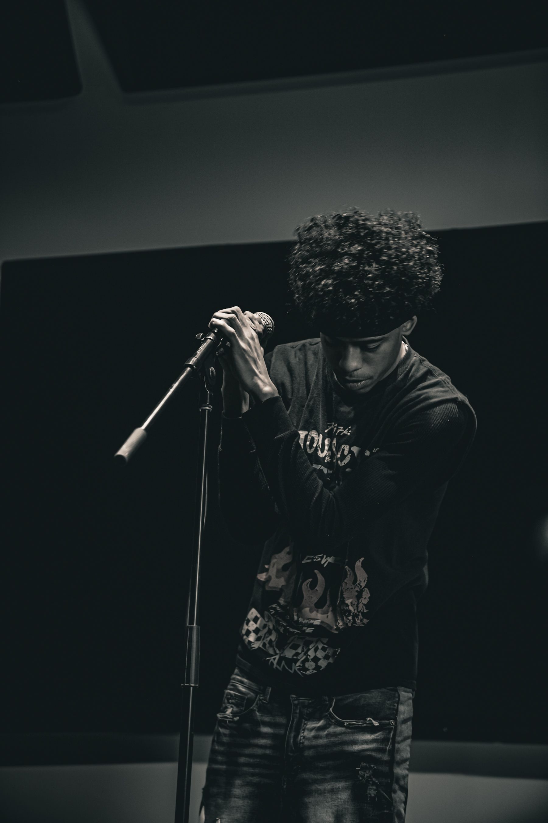 A performer in black clothing grips a microphone on a dimly lit stage.