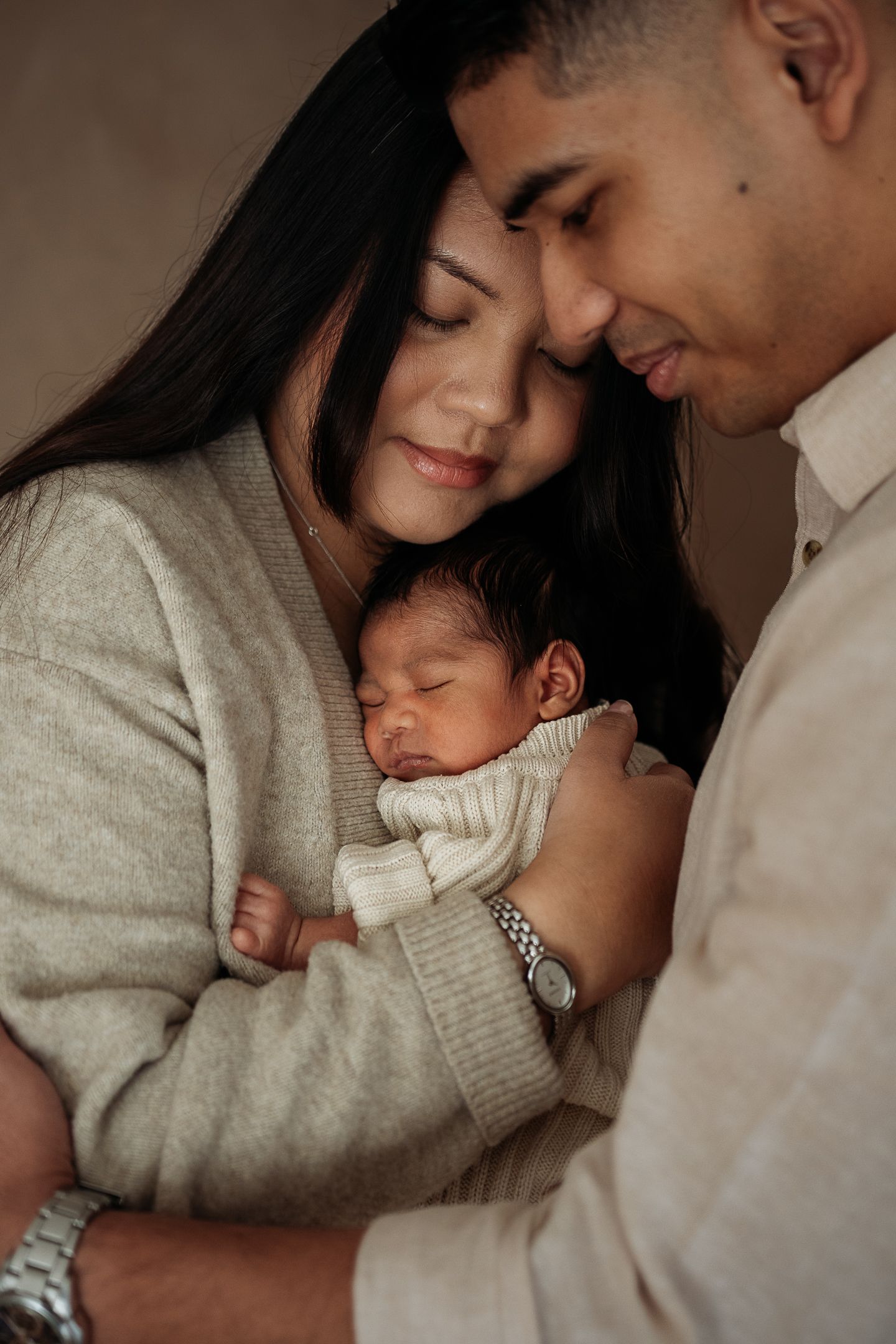 Newborn baby cuddled with both parents softly looking down taken in Penrith newborn studio