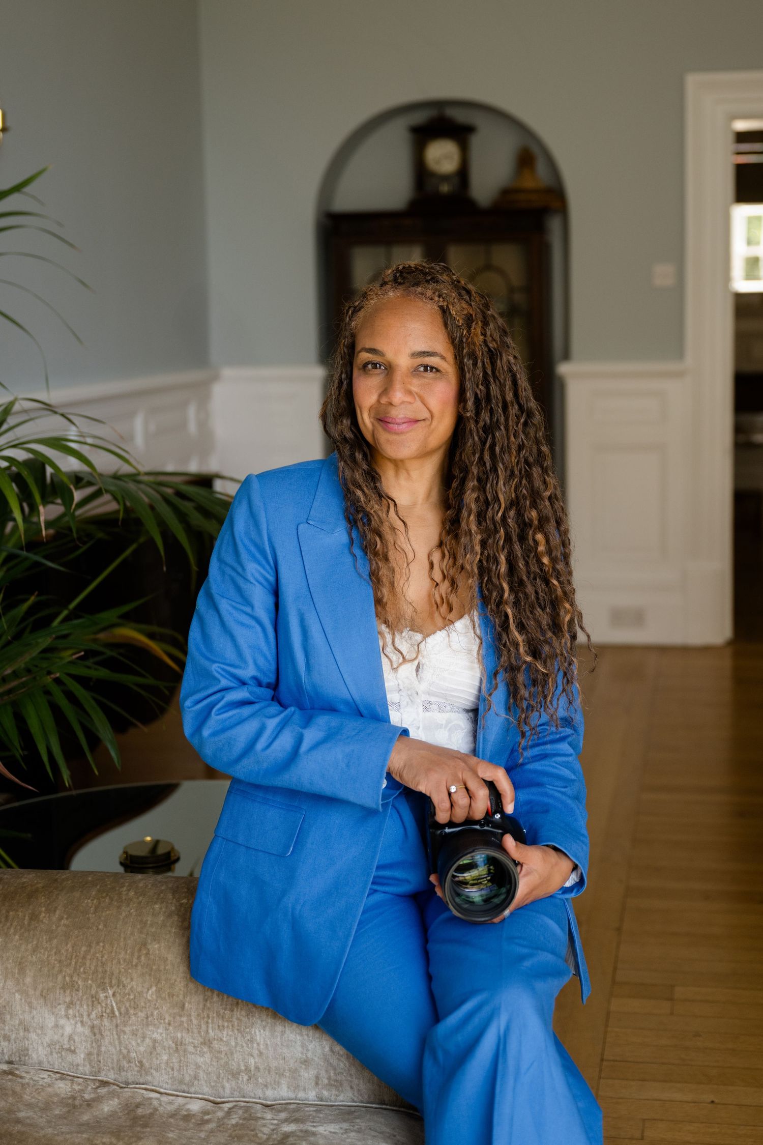Portrait of someone with long locs hairstyle wearing a white top against neutral background.