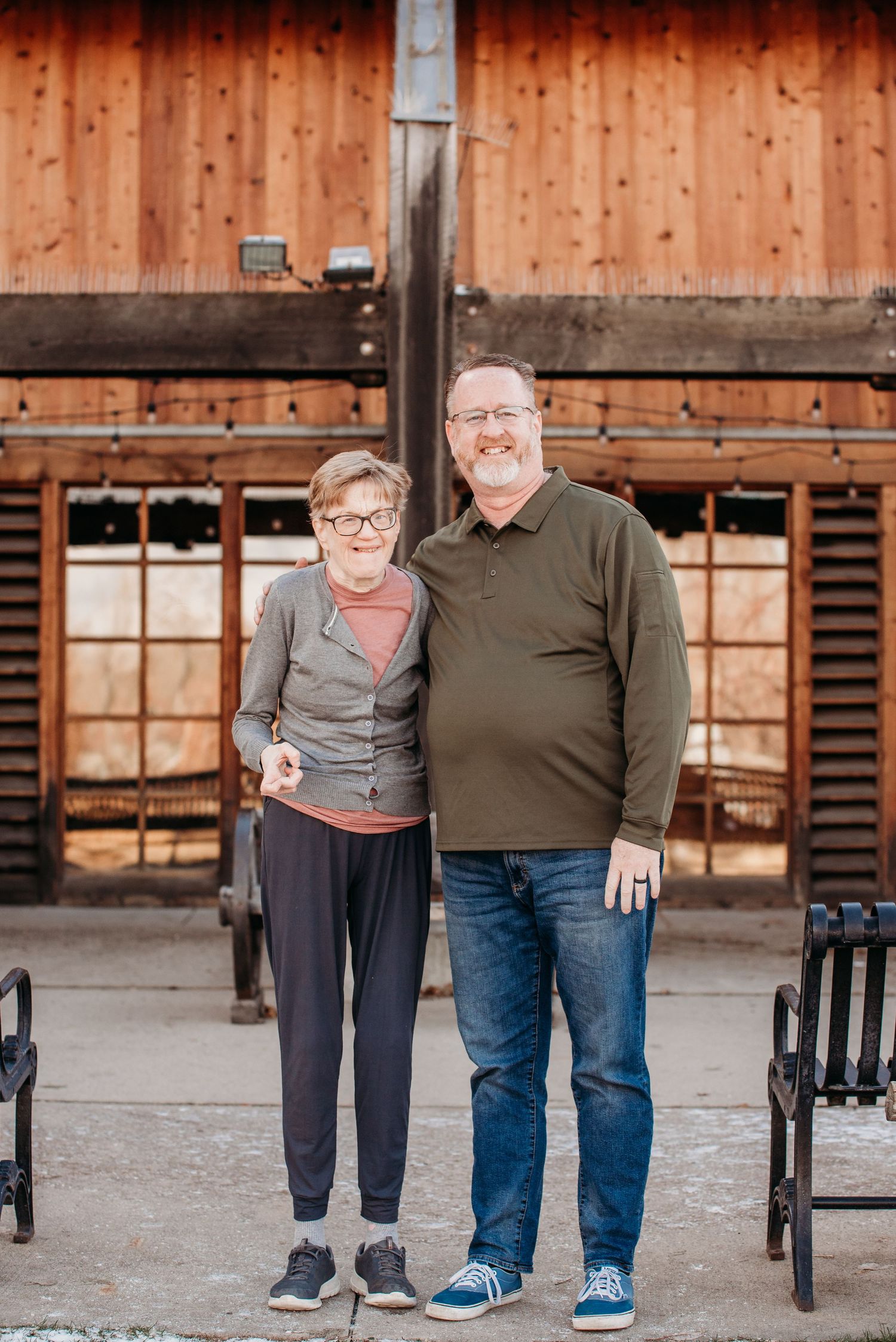 Two people in casual attire standing together in front of a wooden building facade.