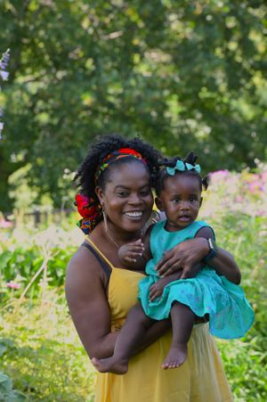 A parent and toddler wearing colorful dresses share a joyful moment together in a sunny garden setting.