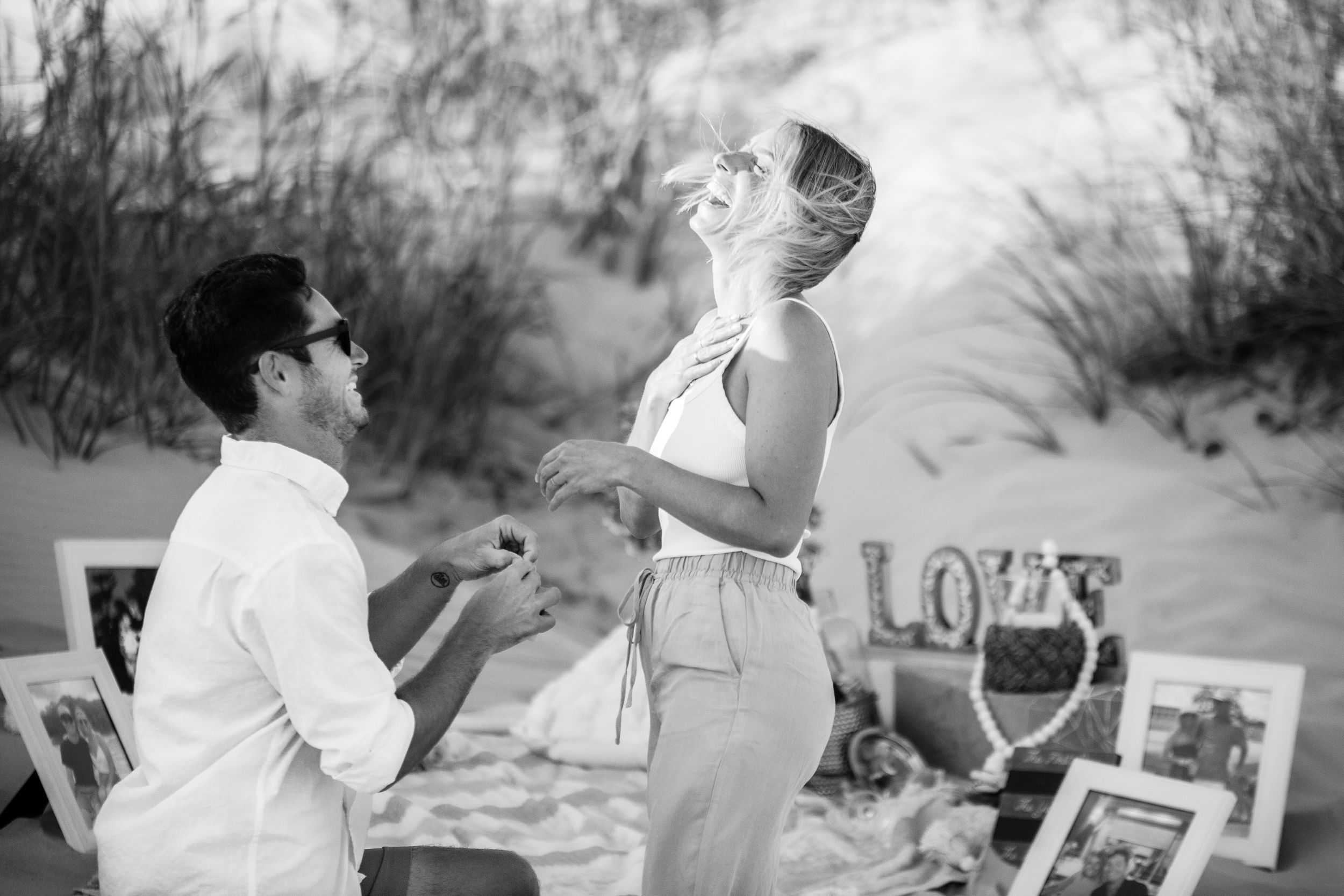 Black and white photo, Candid moment of shock and joy during proposal on the beach, photo by Tasha Cannaday, Windsor Ontario.