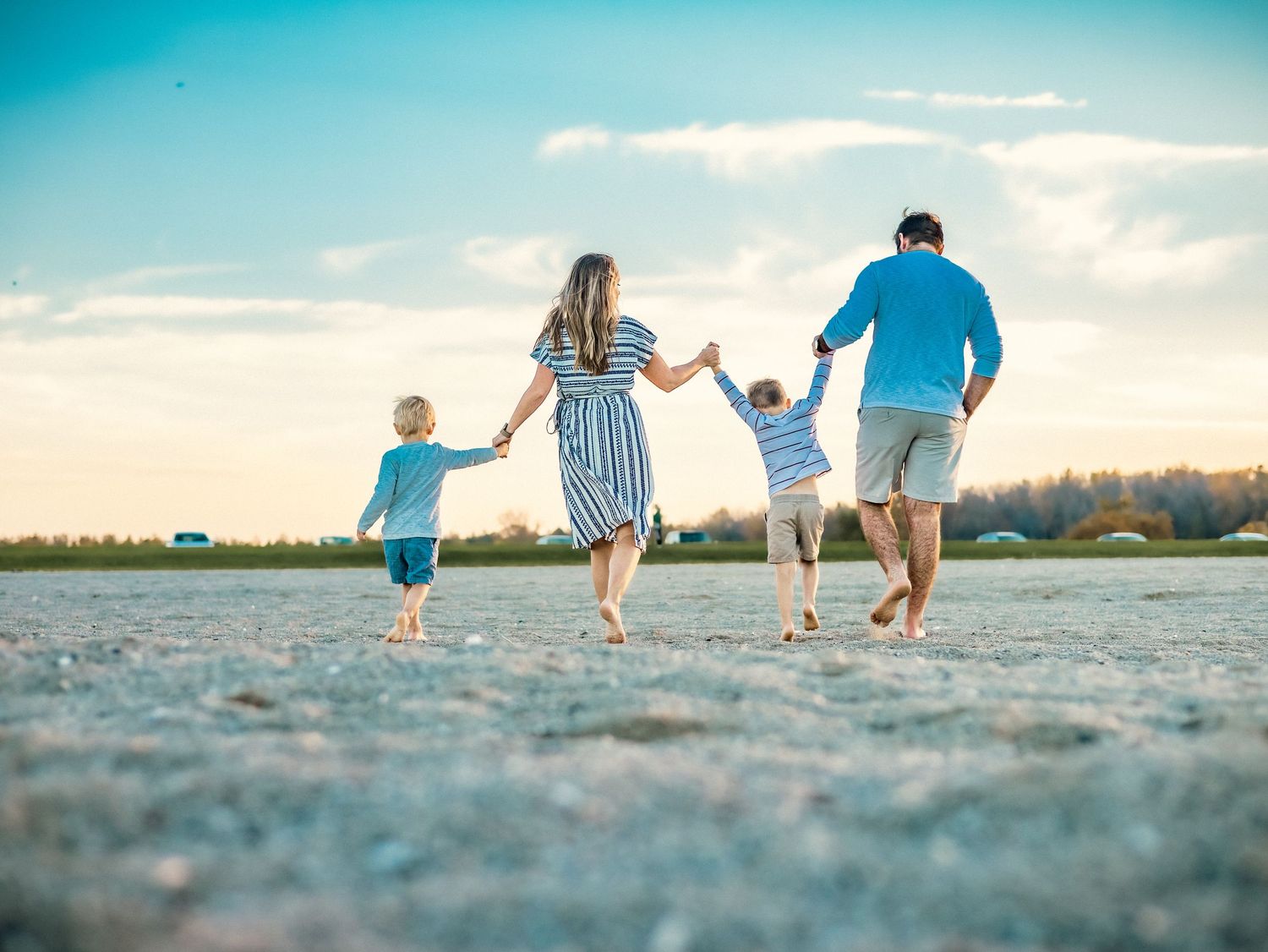 Family holding hands while walking together on a sandy beach during sunset.