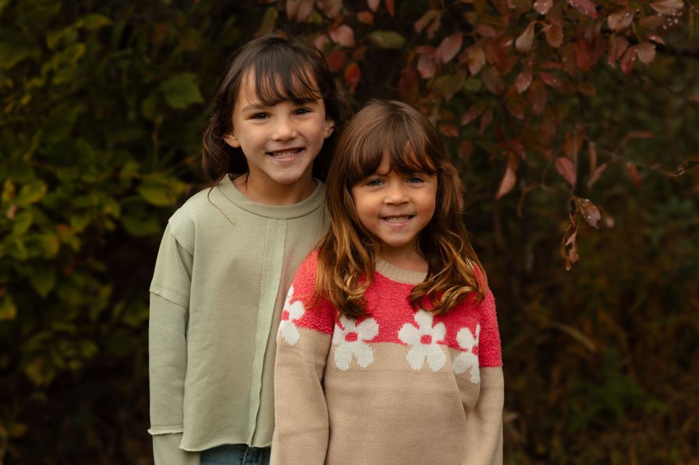 Two young children in casual sweaters smiling together against an autumn background.