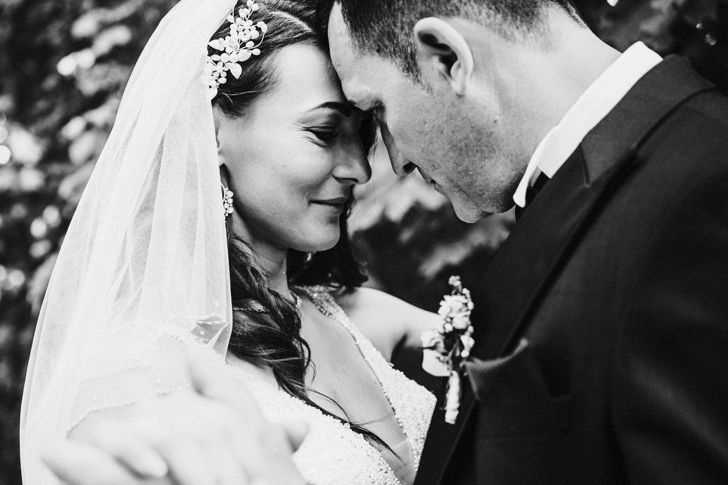 Intimate black and white portrait of newlyweds sharing a tender moment with bride in vintage veil.