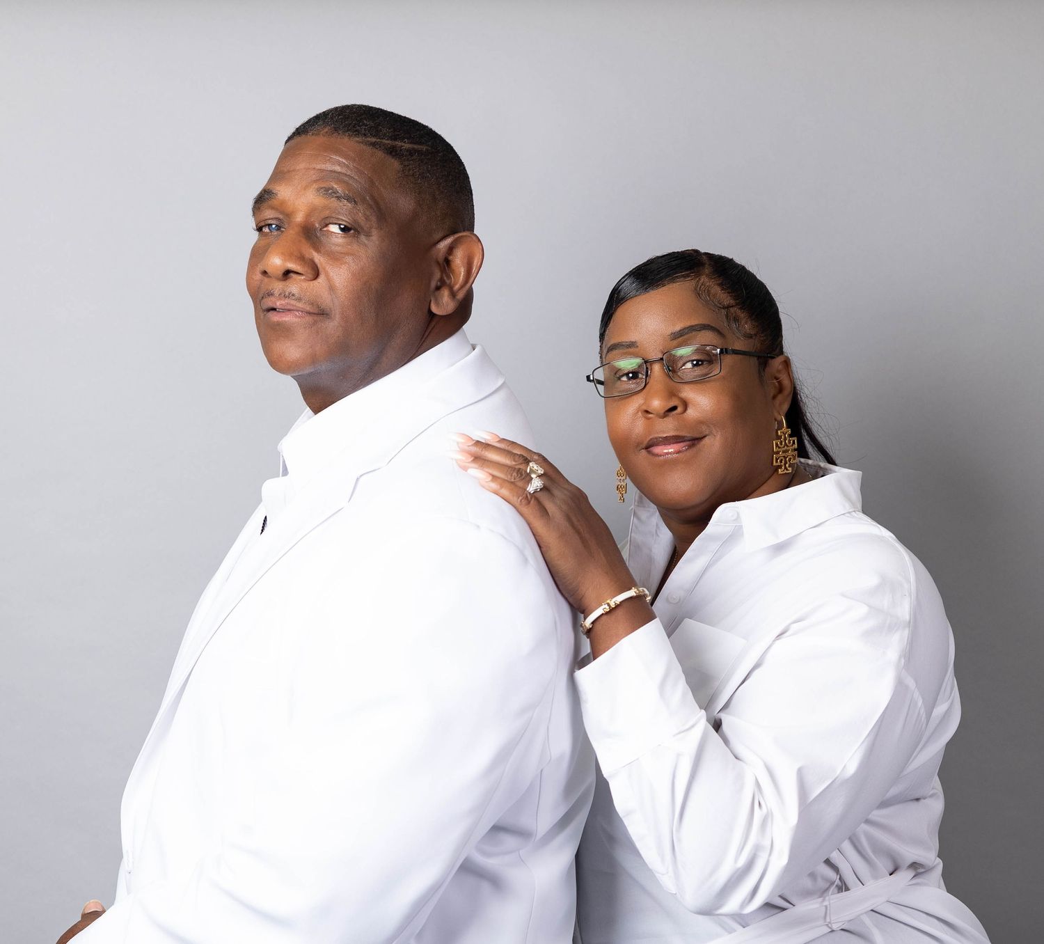 Mature couple in matching white turtlenecks posing back to back in a studio portrait.