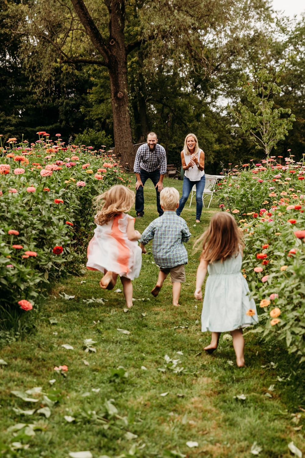 Family running playfully through a garden filled with blooming flowers and greenery.