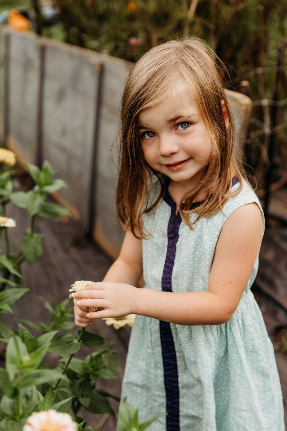 Child wearing a mint dress with navy trim explores a garden setting.