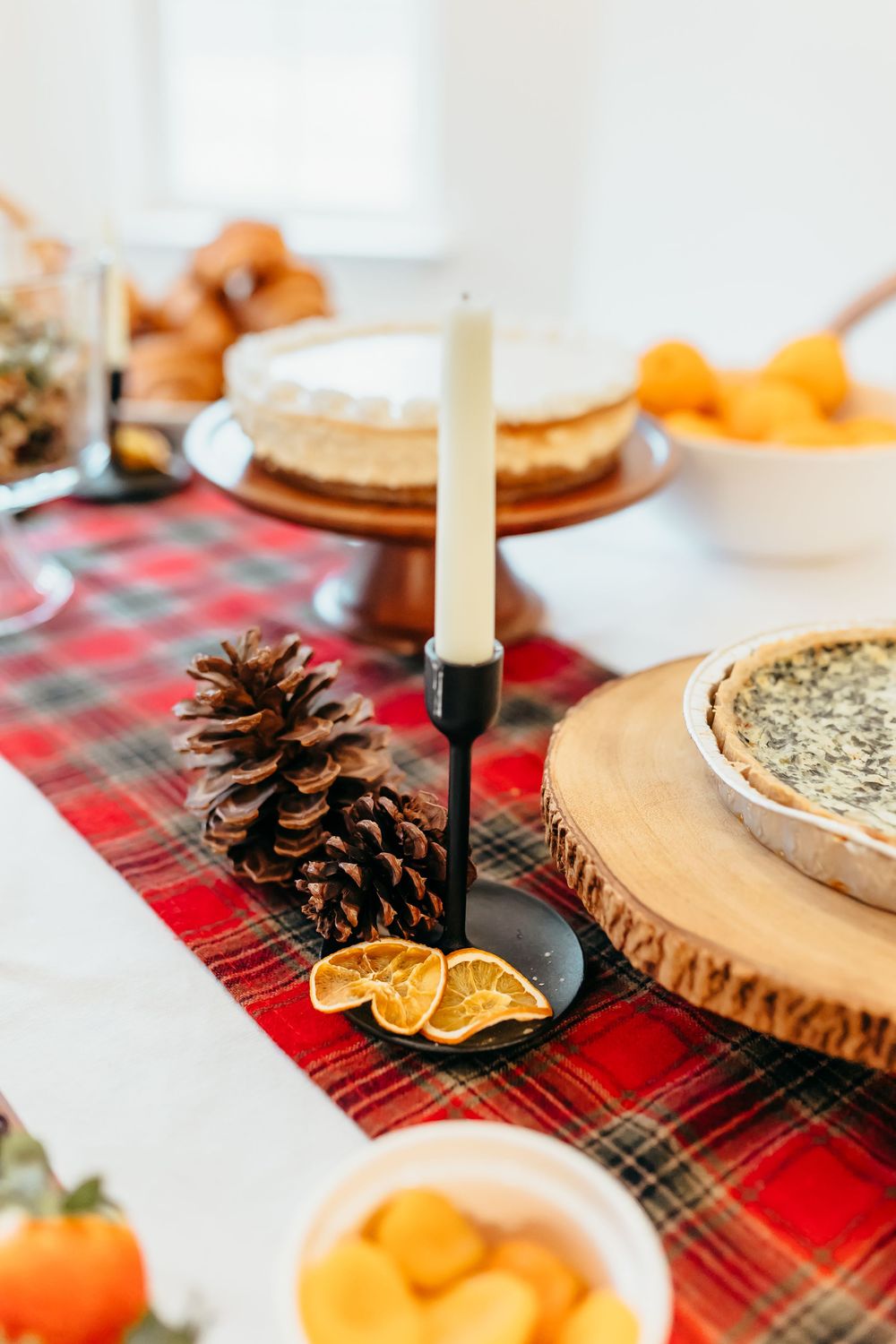 Holiday table setting with plaid tablecloth, pinecones, and white candles for a festive winter gathering.