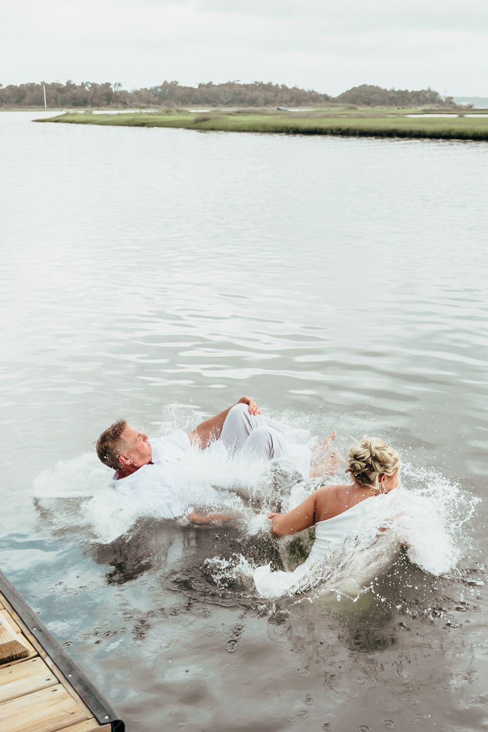 Couple jumping into water fully dressed in wedding attire creating dramatic splashes.