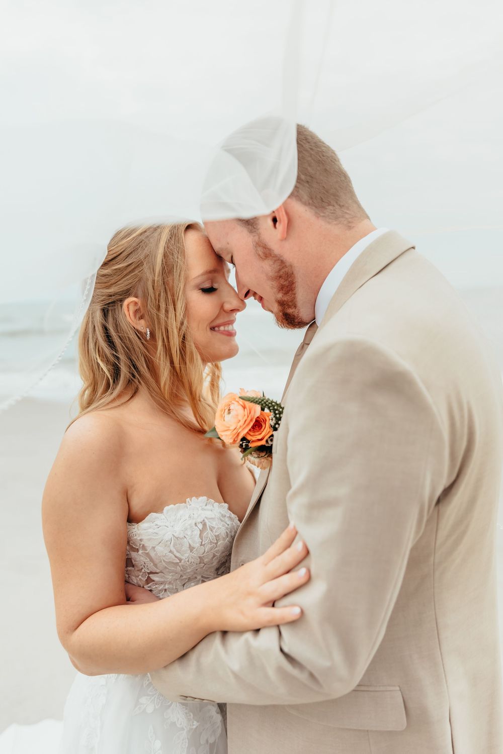 A tender romantic moment shared between a couple in wedding attire near the ocean.