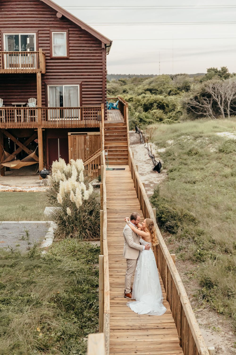 A log cabin beach house with wooden deck overlooking coastal dunes and grasses.