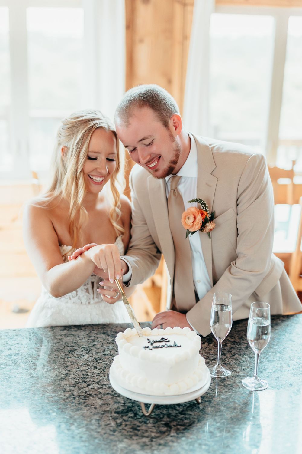 A couple sharing playful moments while cutting their wedding cake on a granite countertop.