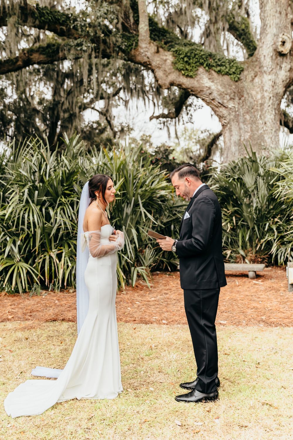 A couple reading handwritten vows beneath a majestic oak tree draped with Spanish moss.