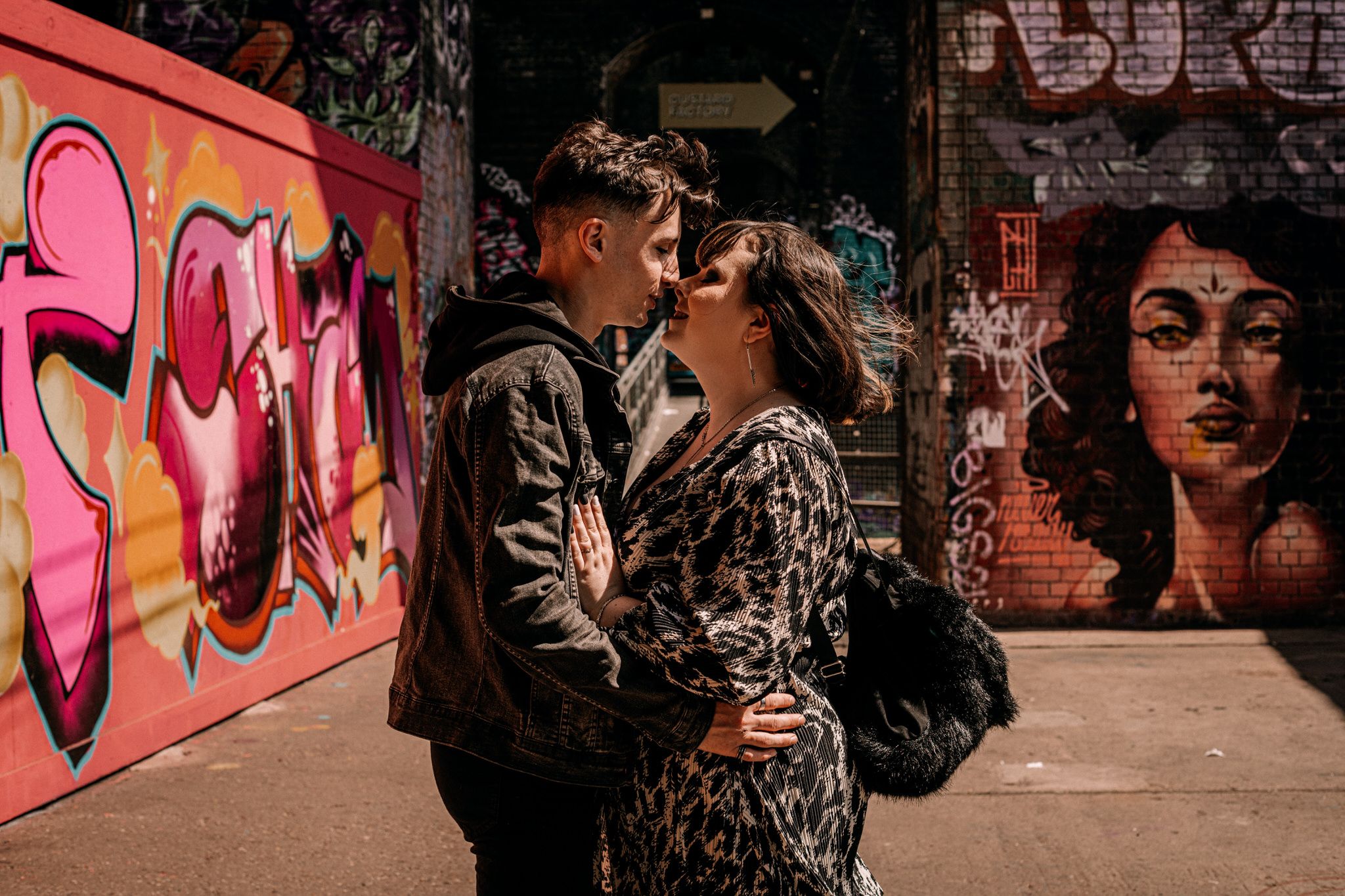Romantic couple sharing a kiss against colorful graffiti wall with urban street art in the background.
