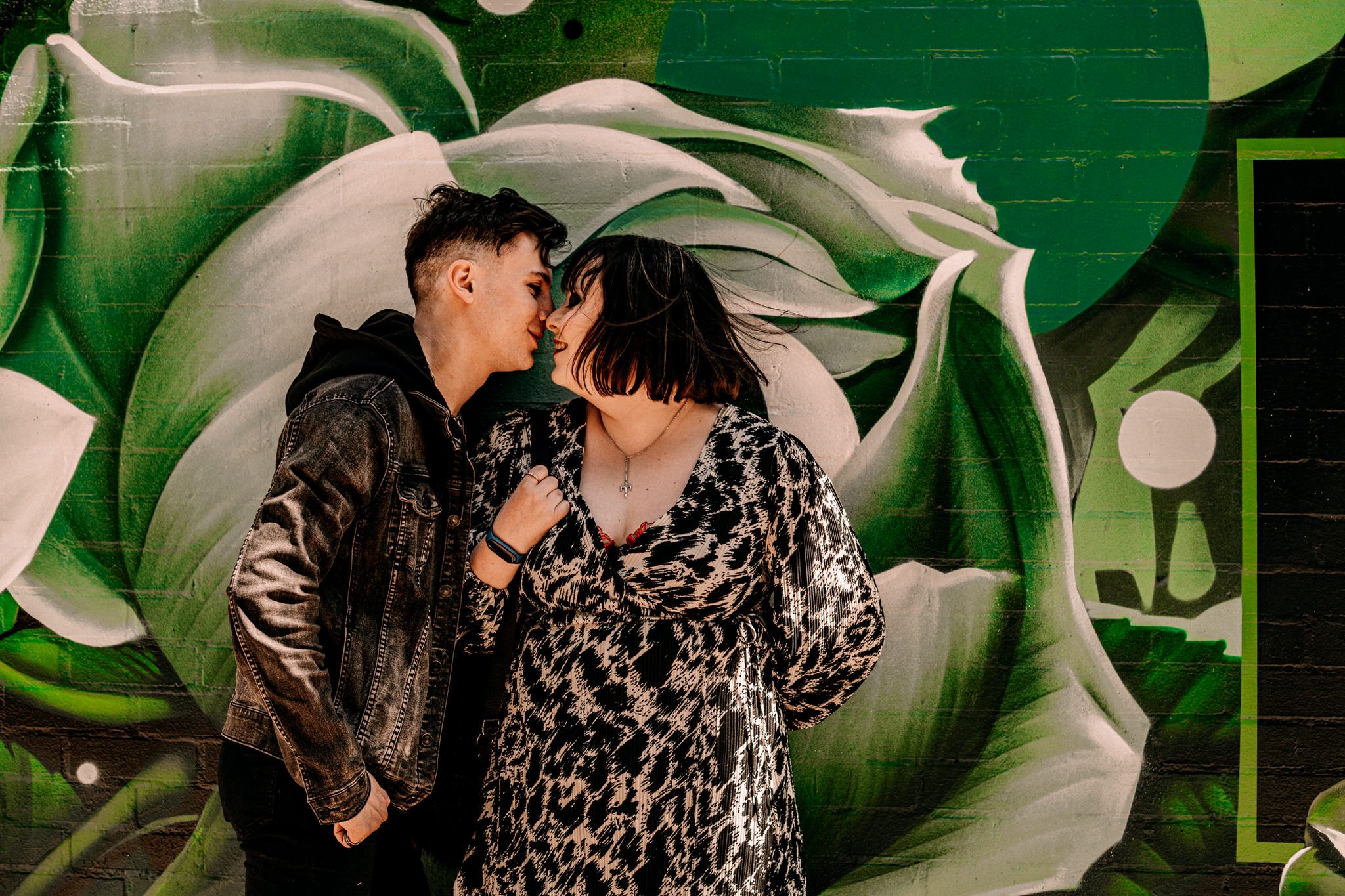 A romantic couple shares an intimate moment against a vibrant green mural wall with floral designs.