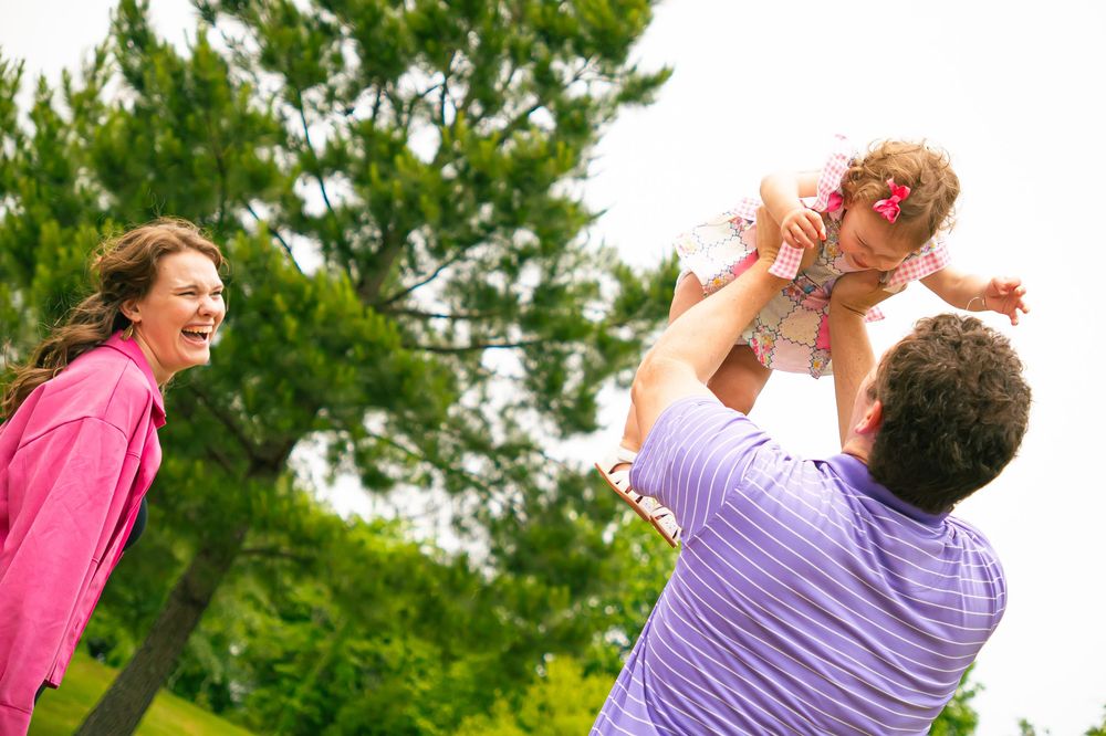 Family enjoying playful moment together in park with green trees in background on sunny day.