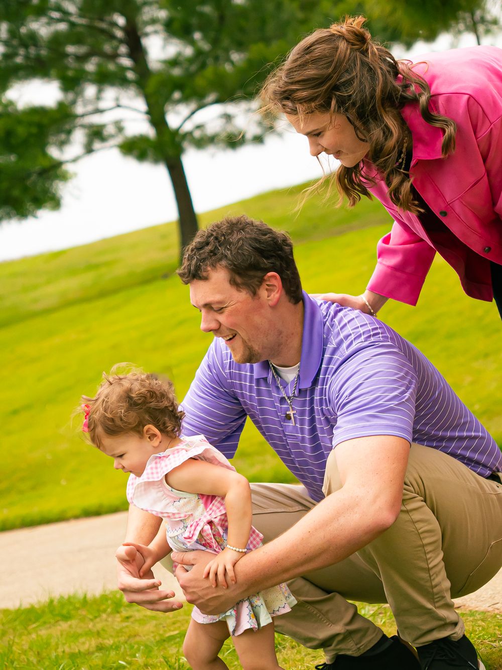 A family enjoying a fun moment together outdoors on a grassy hill with a pink jacket and purple shirt.