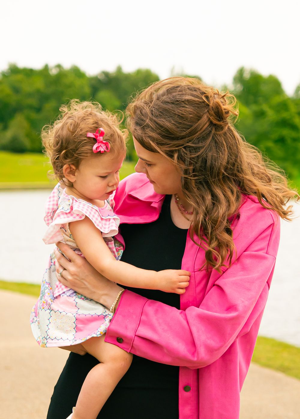 A tender parent-child moment shared outdoors with matching pink outfits and a floral dress.