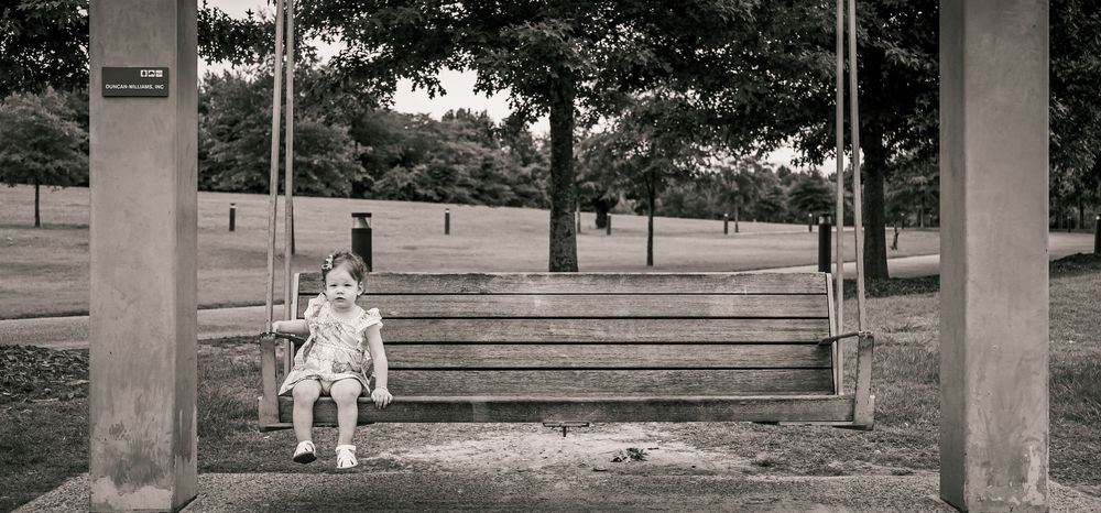 A person in white clothing sits on concrete steps between pillars while viewing a grassy park area.