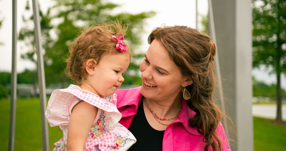 Heartwarming moment between parent and toddler outdoors against a green background.