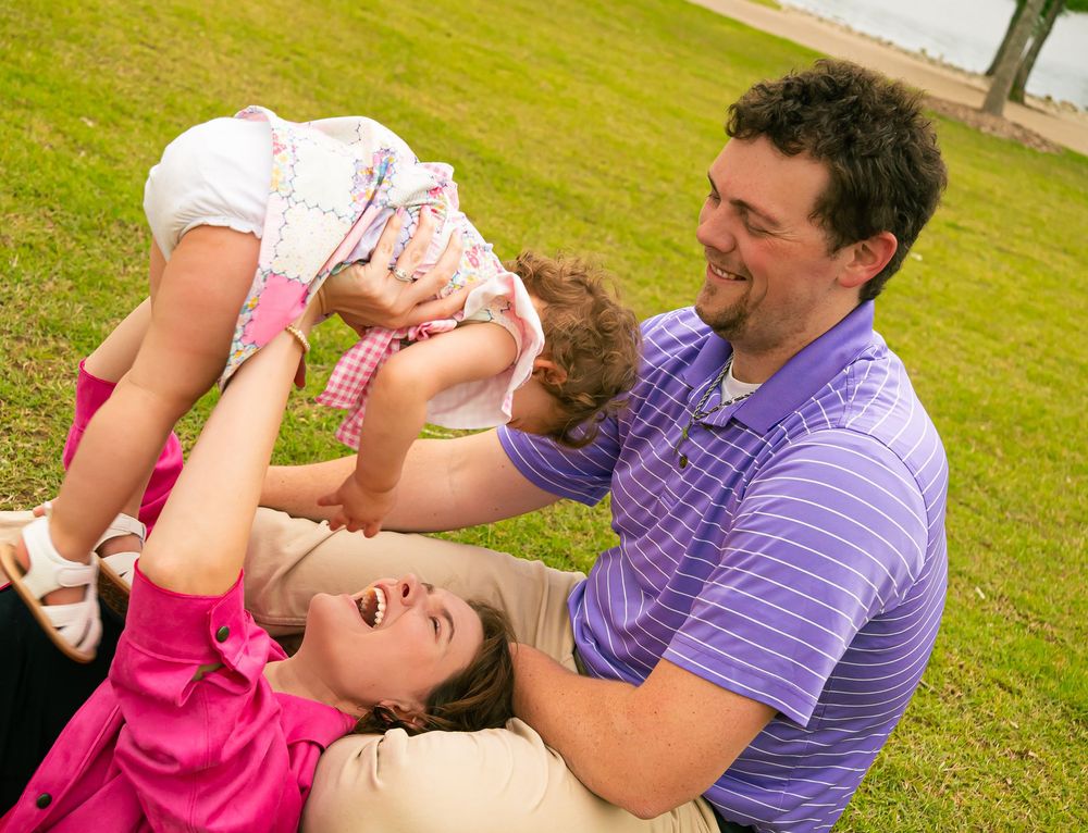 A family plays together and shares joyful moments while laying in the grass on a sunny day.
